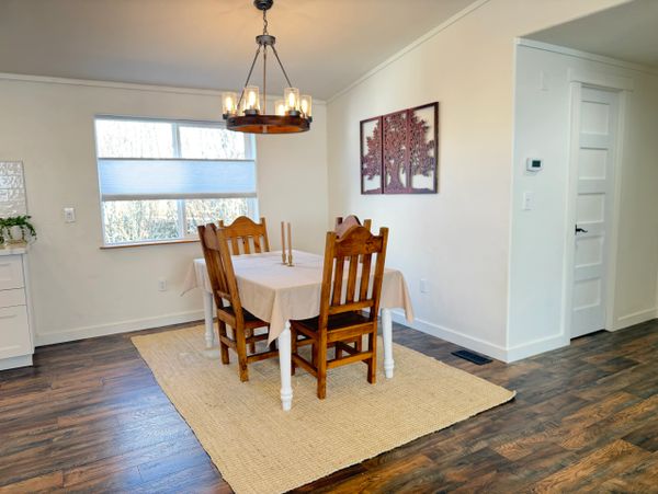 Cozy dining area with wooden chairs, a chandelier, and a neutral rug on wooden flooring.