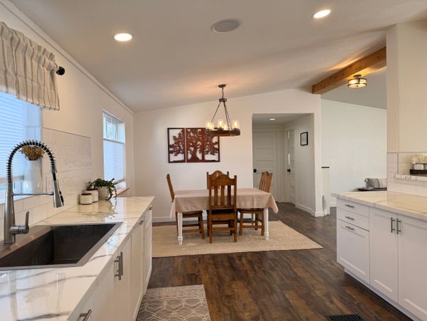 Bright kitchen with white cabinets and wooden dining set under chandelier.