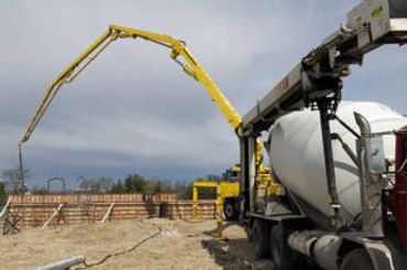 A yellow and white concrete pump truck delivers concrete on a construction site.
