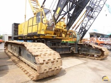 A close-up of a large yellow crawler crane's tracks and lower body.