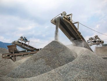A conveyor belt at a quarry deposits a pile of crushed gravel under a cloudy sky.