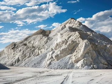 A large pile of white aggregate material in a quarry against a blue, cloudy sky