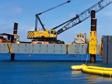 A large yellow crane on a barge uses its boom next to a tall, yellow structure.