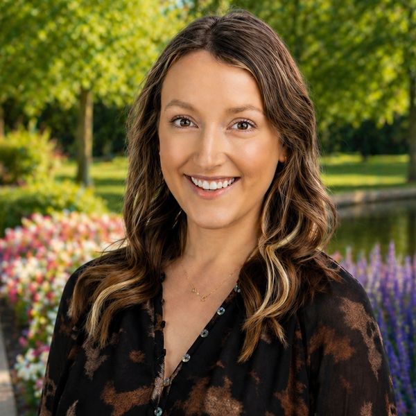 Smiling woman with wavy hair outdoors in a vibrant garden.