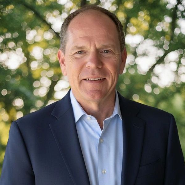 Middle-aged man in a blue suit outdoors with blurred greenery background.