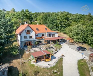 Spacious countryside house with orange roof surrounded by greenery and parking area.