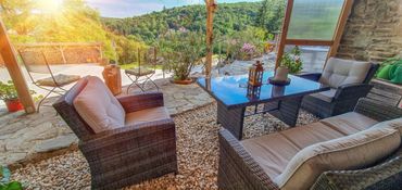 Cozy outdoor seating area with cushioned chairs and a glass table overlooking a lush green landscape.