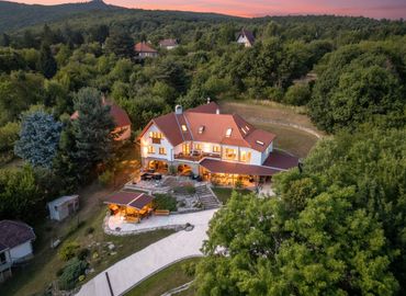 A large, illuminated house surrounded by dense greenery at sunset.