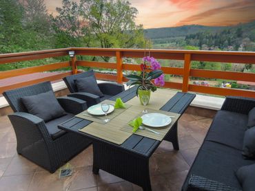 Outdoor dining set on a terrace with a scenic view at sunset.