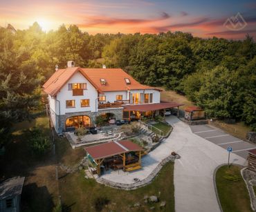 Cozy countryside house with a red roof at sunset surrounded by trees and parking space.