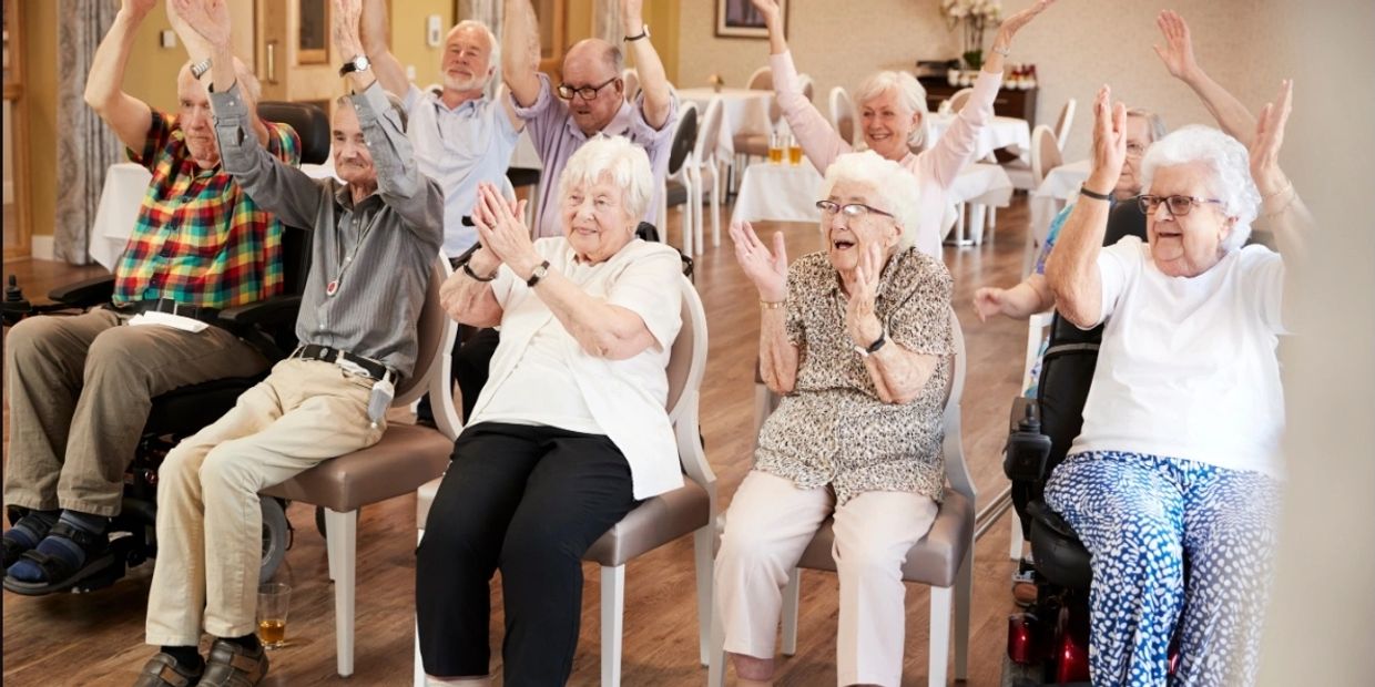 Elderly group enjoying a seated exercise session with raised arms and smiles.