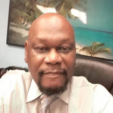 Man in a tie sitting in an office with tropical artwork behind.