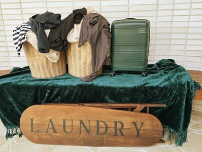 Two laundry baskets and a suitcase on a green cloth with a laundry sign.
