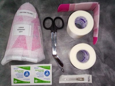 Ear piercing kit with labeled pendant, scissors, tape, alcohol pads, and needle.