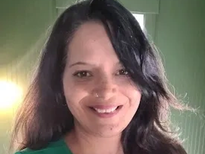 A woman smiling indoors with light green walls.