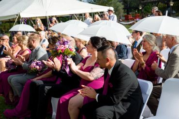 Wedding guests applauding under white umbrellas.