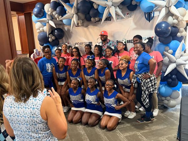 A group photo of cheerleaders and supporters posing in front of a blue and white balloon arch.