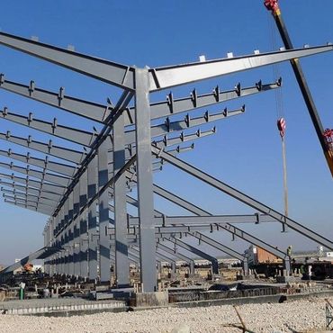 Steel framework of a large building under construction with a crane on site.