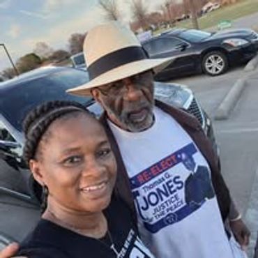 Two people smiling outdoors, one wearing a hat and a graphic t-shirt.