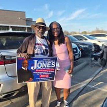 Two people holding a campaign sign for Jones in a parking lot.