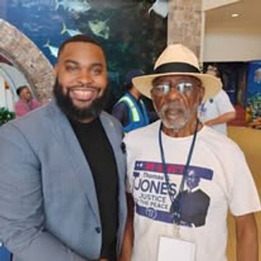Two men smiling, one in a suit and the other in a campaign T-shirt and hat.