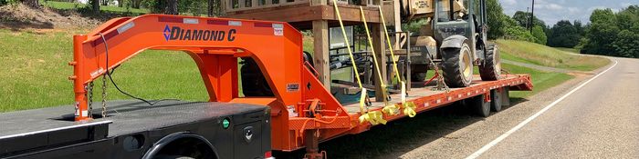 Orange Diamond C trailer carrying a forklift secured with yellow straps.