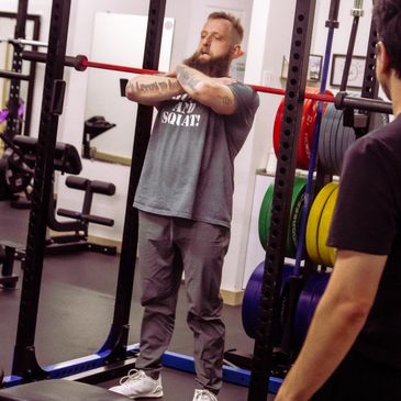 Man performing a front squat in a gym with a barbell on his shoulders.