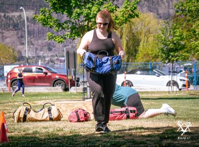 Woman carrying a blue bag outdoors with exercise equipment around.