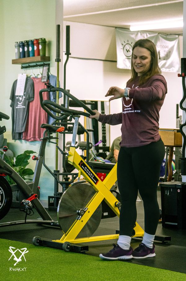 A woman in workout clothes standing next to a yellow stationary bike in a gym.