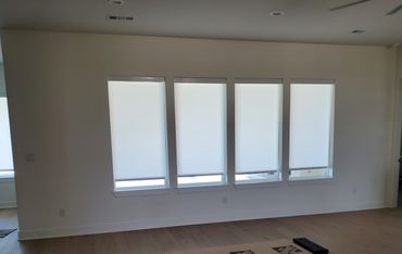 Four windows with white roller shades in a modern room.