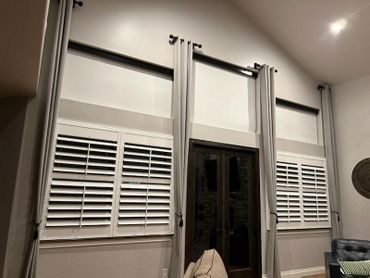 Tall windows with white shutters and beige curtains in a modern living room.