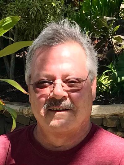 Man with glasses and mustache in a garden setting.