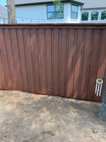 Brown wooden fence with string lights and wind chimes in backyard.