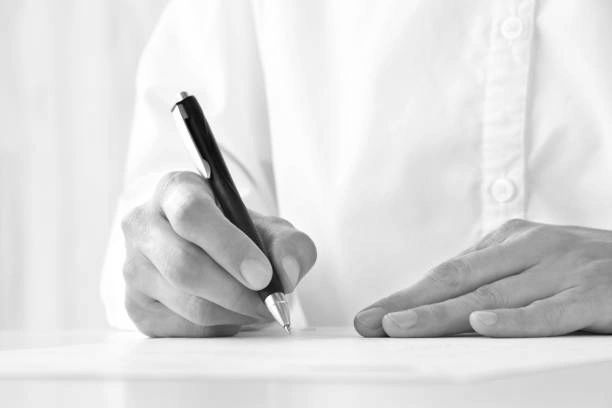 Person writing on paper with a black pen, wearing a white shirt.