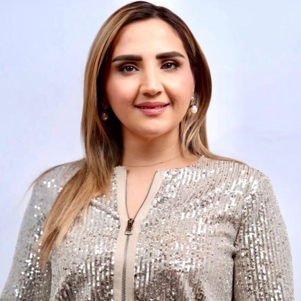 Portrait of a smiling woman in a sparkling silver top with pearl earrings.