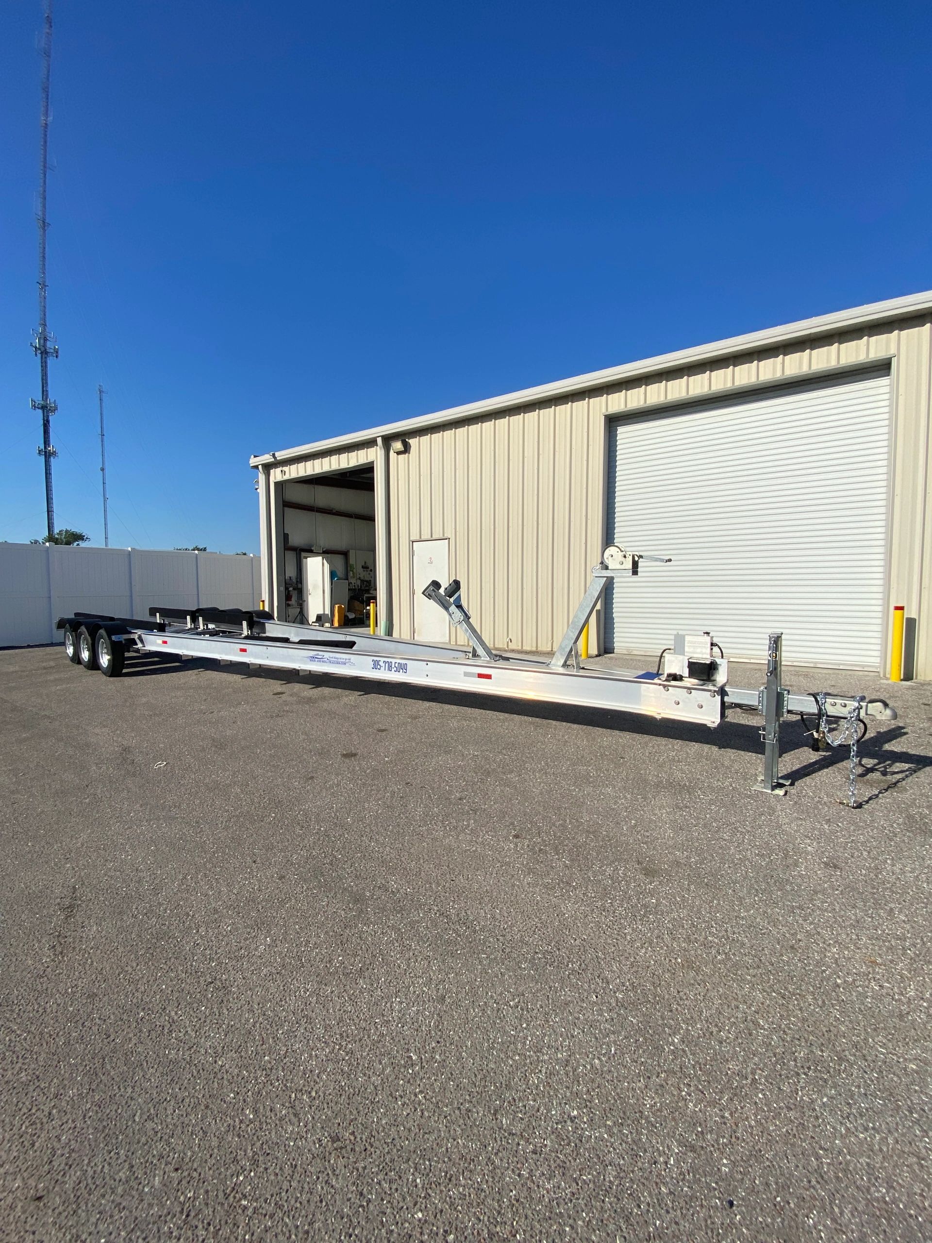 Long aluminum trailer with triple axles parked outside a warehouse.