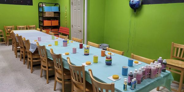 A long table set up for a children's art activity in a bright green room.