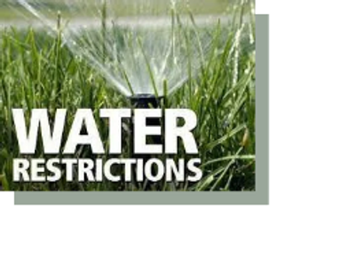 Photo of a lawn sprinkler running with the words "Water Restrictiions"