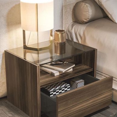 Modern wooden bedside table with lamp, books, and decorative boxes in a cozy bedroom.