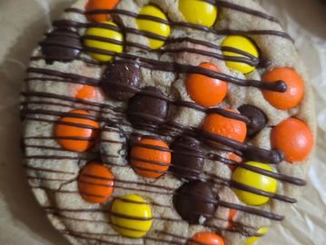 Cookie with colorful candy pieces and chocolate drizzle on parchment paper.