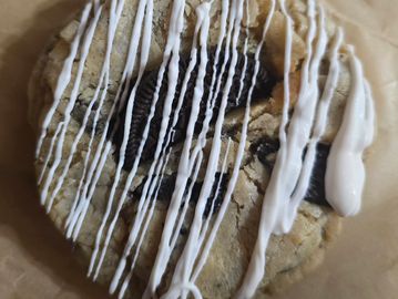 Cookie with Oreo pieces and white icing drizzle on parchment paper.