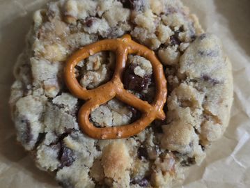 A chocolate chip cookie topped with a pretzel on parchment paper.