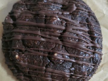 A large chocolate cookie drizzled with chocolate on parchment paper.