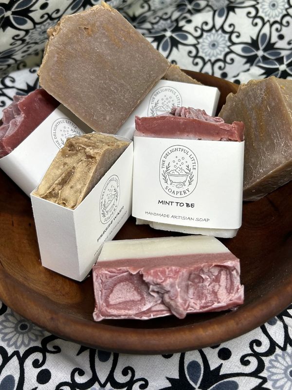 Artisan handmade soaps in a wooden bowl with decorative labels.