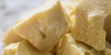 Close-up of chunks of beige cocoa butter on a textured surface.