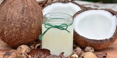 A jar of coconut oil with whole and halved coconuts on wooden surface.