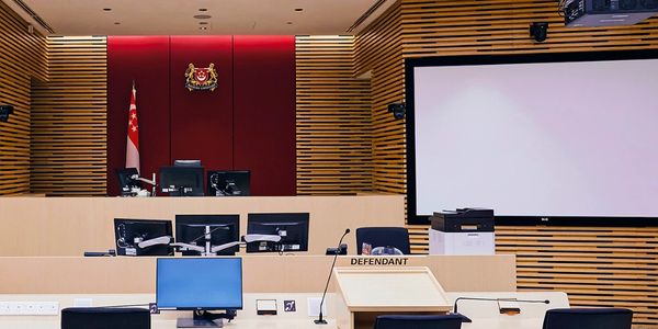 Modern courtroom with defendant's area and large screen, featuring Singapore's flag and coat of arms.