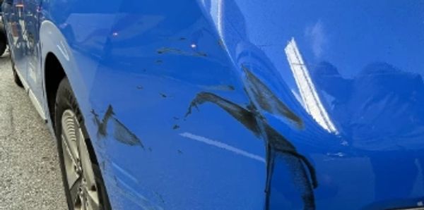 Blue car with a large dent and scratches on the rear side panel.