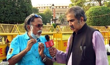 A man in blue shirt being interviewed outdoors by a reporter holding a microphone.