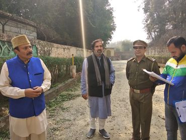 Four men, including a police officer, stand outdoors on a sunny day.